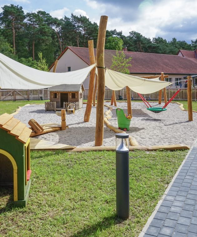 Sicht auf den Spielplatz, im Vordergrund ein kleines, grünes Spielhaus