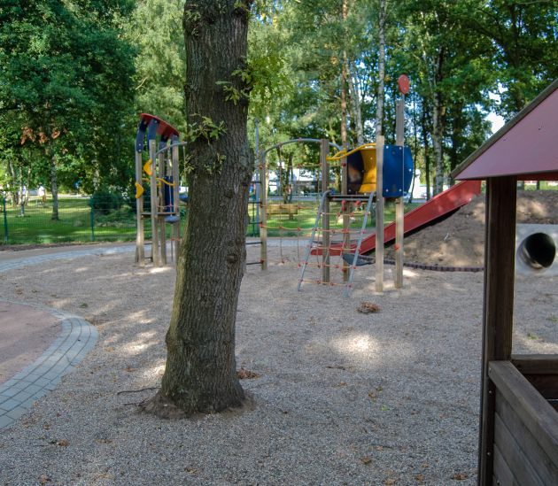 Spielplatzansicht mit Baum im Vorder- und Wald im Hindergrund