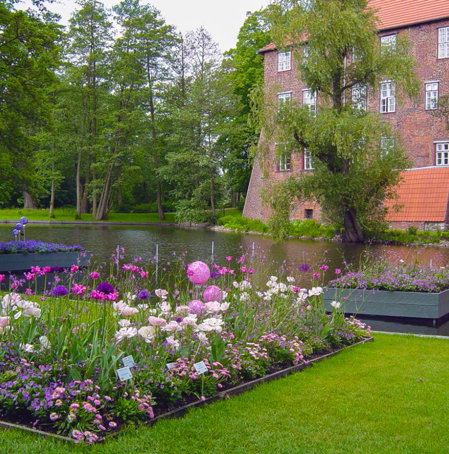 Blumenbeet auf einer Wiese angrenzend an dem Kanal vor dem Ziegelsteingebäude